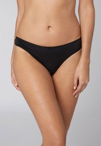Slip bikini nero realizzato in tessuto morbido con una texture liscia, caratterizzato da un taglio a vita bassa e una vita sottile, impreziosito da un piccolo fiocco.