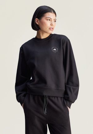 Zwarte sweatshirt met lange mouwen, geribbelde manchetten en onderrand, voorzien van een rond logo op de borst. Gecombineerd met bijpassende zwarte broek.