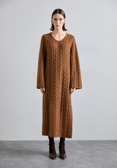 Abito lungo in maglia cable knit marrone con scollatura a V e maniche lunghe, realizzato in un filato spesso e testurizzato. Presenta una vestibilità comoda e rilassata.