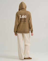 Felpa con cappuccio marrone con i loghi bianchi "Lee" e "Crayola" sulla schiena. Abbinata a pantaloni larghi color crema e calzature marroni.