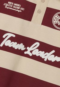 Bordeaux- und beigefarbenes gestreiftes Poloshirt mit drei Knöpfen; mit gesticktem "Team Loader" und Wappen mit "North America Athletic Season 1923".