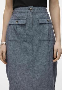 Tummansininen midihame denim-kankaasta, jossa on hieman teksturoitu pinta. Hameessa on kaksi etutaskua ja kaksi metallinappia vyötäröllä.