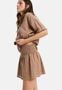Bruine textuuroutfit met een losse top en een gestikte rok met een uitlopende zoom, die cirkelvormige patronen en lichte stof accentueert.