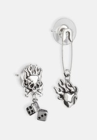 Silver earrings featuring a skull with flames, a dangling pair of dice, and a heart with flames. Clip-on and stud design with metallic finish.
