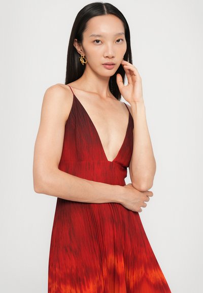 Robe rouge avec un décolleté en V profond et des fines bretelles, présentant un design dégradé passant d'un rouge foncé à un orange. La texture plissée accentue l流e.
