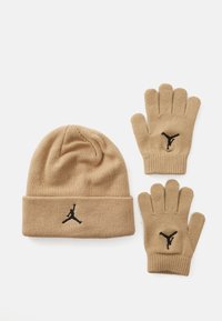 Bež pleteni šešir i odgovarajuće rukavice s crnim izvezenim Jumpman logom na bijeloj pozadini.