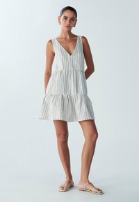 Paski mini sukienka z dekoltem w kształcie litery V, z warstwowym krojem, wykonana z lekkiego materiału z pionowymi niebieskimi i szarymi paskami. Dobrzona z beżowymi sandałami.