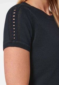 Navy-blaues Strickoberteil mit kurzen Ärmeln, das ein strukturiertes Muster und kleine Aussparungen entlang der Schulternaht aufweist.