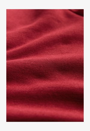 Red fabric with a smooth texture, displaying subtle weave patterns and gentle folds, indicating softness and drape.