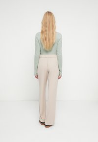 Mintgroen topje met lange mouwen en een losse pasvorm, gecombineerd met beige broek met wijde pijpen en een elastische tailleband. Gladde textuur.