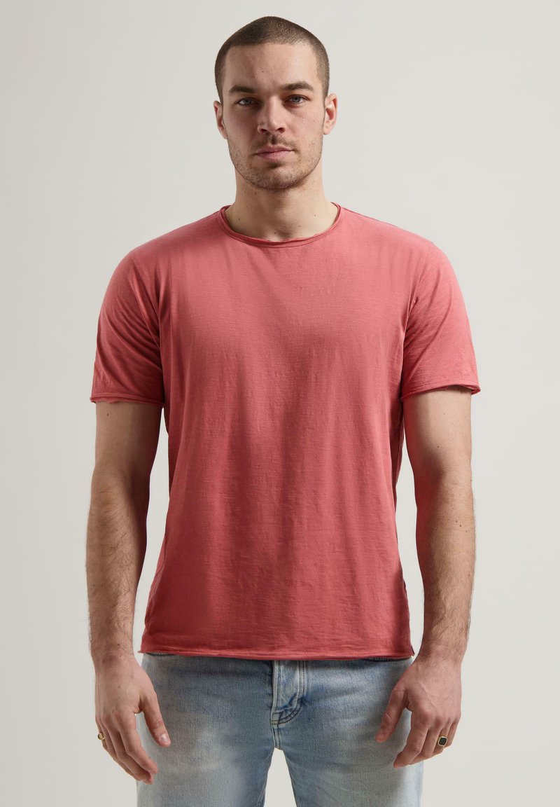Tricou cu mânecă scurtă, guler rotund, din bumbac corai, cu o suprafață ușor texturată și detalii cu cusături vizibile de-a lungul gulerului.