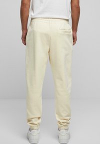 Light cream sweatpants made from soft fabric, featuring an elastic waistband, cuffed ankles, and a back pocket detail.
