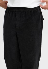 Black corduroy pants with an elastic waistband, featuring a textured surface and side pockets for practicality and comfort.