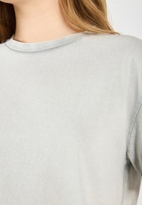 Light gray crew neck t-shirt made of soft, smooth fabric. Features short sleeves and a subtle texture with minimal seams.