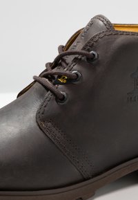 Pruun nahkne pahkluu saabas, millel on sile tekstuur, ümmargune nina, õmmeldud detailid ja tumedad paelad, mis on läbi metallist silmade keeratud.