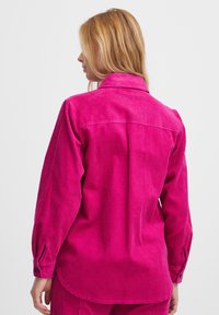 Fuchsia Corduroy-Hemd mit Kragen, langen Ärmeln und Knopfmanschetten. Verfügt über eine vertikale Rippstruktur und einen abgerundeten Saum.