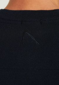 Maglione lavorato a maglia blu navy con una texture a coste, caratterizzato da un piccolo filo allentato vicino al collo. Design semplice con colletto rotondo.