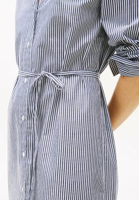 Abito a righe blu navy e bianco, con vita legata e maniche voluminose. Il materiale è cotone leggero con una texture liscia.