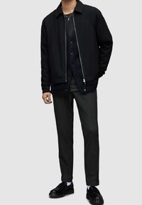 Czarna marynarka w prążki z zamkiem błyskawicznym i kołnierzem, nałożona na ciemnoszary warstwowy strój. Połączona z ciemnymi spodniami i czarnymi butami. Prosty, teksturowany wzór.