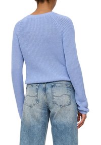 Helles blaues Strickpullover mit einem gerippten Rundhalsausschnitt und langen Ärmeln, getragen mit hellblauen, hoch geschnittenen Jeans mit Gesäßtaschen.