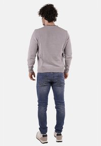 Maglione grigio chiaro lavorato a maglia con scollatura rotonda, abbinato a jeans di denim blu. L'outfit presenta una vestibilità morbida e polsini a coste.