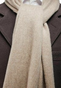 Beige uldscarf draperet over en mørkebrun frakke, med en blød tekstur og en glat, ensartet finish. Designet er enkelt og klassisk.