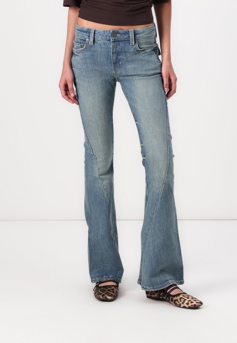 Light blue denim flared jeans with a faded finish, classic five-pocket design, and subtle whiskering details. Styled with black and beige shoes.