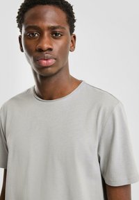 Jasnoszara koszulka z krótkim rękawem wykonana z gładkiej tkaniny, z okrągłym dekoltem i subtelną fakturą na powierzchni.