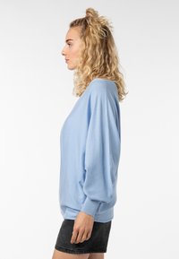 Hellblaues, übergroßes Sweatshirt mit gerippten Bündchen, das eine weiche Textur und lässige, fallende Schultern aufweist, kombiniert mit einem schwarzen Minirock.