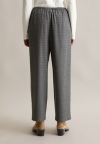 Grijze geruite broek met een losse pasvorm en een elastische tailleband, met subtiele rode en blauwe lijnen. Draag met open schoenen.