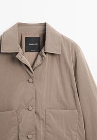 Light brown jacket with a collared neckline, front buttons, and two large pockets. Made of textured fabric with a soft sheen.