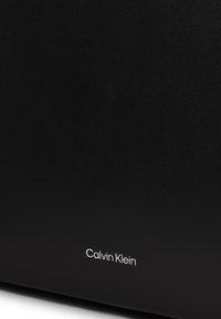 Borsa in pelle nera con una superficie liscia e un design minimalista. Logo "Calvin Klein" in argento, impresso nella parte inferiore.