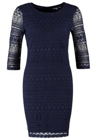 Robe en dentelle bleu marine avec des manches trois-quarts, présentant des motifs complexes et une silhouette ajustée. Texturée avec un ourlet en dents de scie.