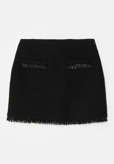 Črna krilo z teksturirano tkanino, ki ima dva sprednja žepa in rob z resicami. Splošna oblika je prilegajoča A-linija.