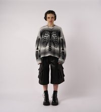 Pārlieku liels pelēks džemperis ar melnu skeleta grafiku, kombinēts ar melniem kravas šortiem ar slāņveida kabatām un melniem stingriem zābakiem.