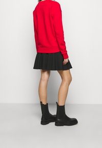 Sudadera roja, falda corta negra con pliegues y botas negras de tobillo con suela texturizada. El atuendo presenta colores contrastantes y un diseño casual.