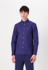 Camisa de botones de manga larga azul marino con corte recto, botones blancos y un pequeño logotipo amarillo bordado en el pecho. Material de algodón.