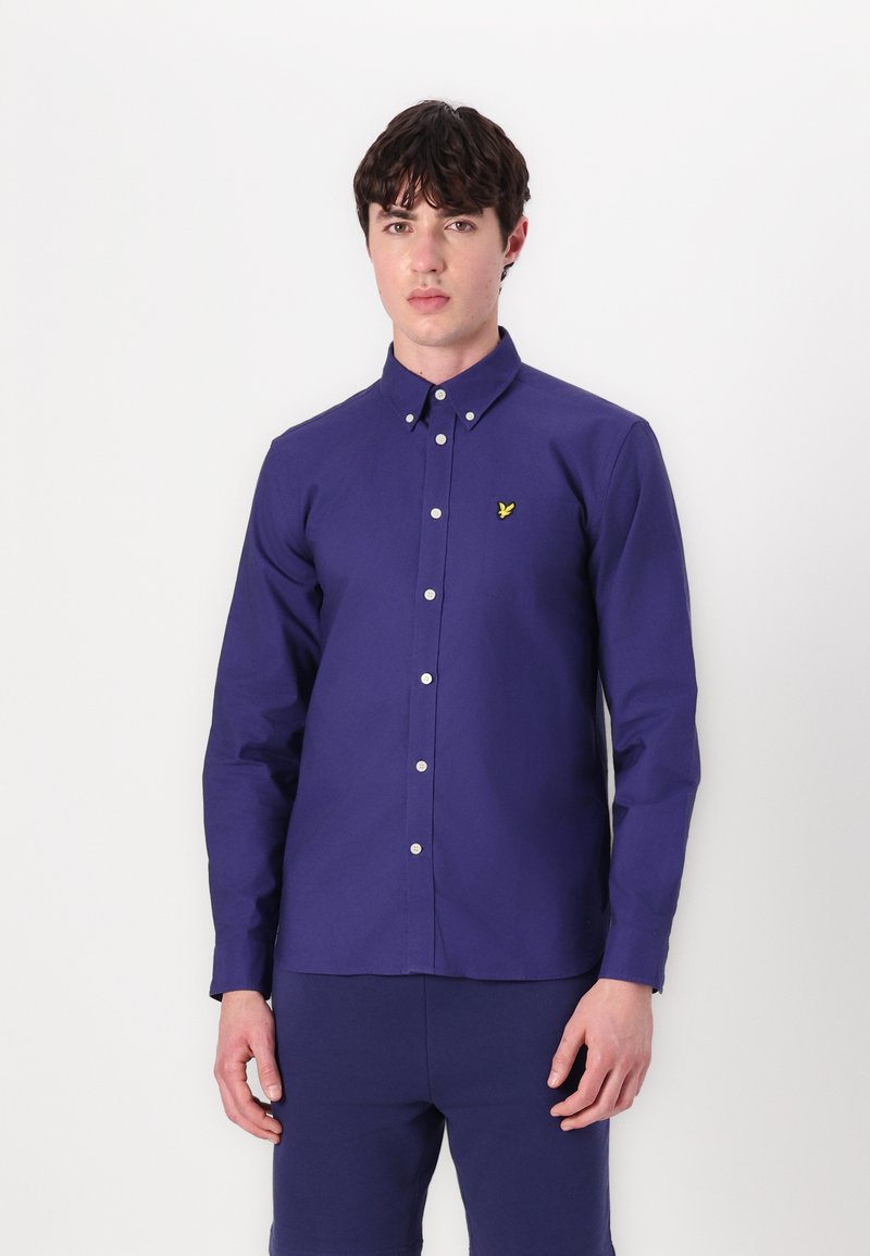 Camisa de botones de manga larga azul marino con corte recto, botones blancos y un pequeño logotipo amarillo bordado en el pecho. Material de algodón.