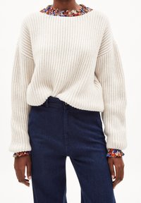 Maglione crema a coste con un nodo sul davanti, presenta un colletto a fantasia floreale colorato e maniche ampie, abbinato a jeans blu scuro.