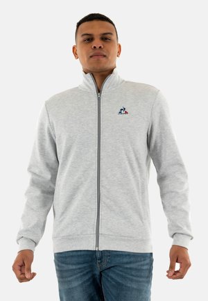 Gray zip-up sweatshirt in a soft material, featuring a high collar and logo on the left side, paired with blue denim jeans.