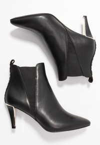 Svarta ankelboots med spetsiga tår, i lädermaterial, elastiska sidopaneler och en metallisk häldetalj. Slät textur utan synliga mönster.