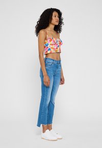 Top floreale corto con spalline sottili, abbinato a jeans chiari a vita alta con orlo sfilacciato e sneakers bianche.