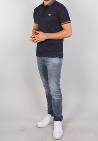 Laivastonsininen poolopaita, jossa on geometrinen kuosi, lyhyet hihat, punavalkoraidallinen kaulus, yhdistetty vaaleansinisiin farkkuihin ja valkoisiin tennareihin.