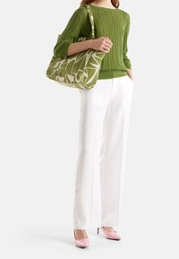 Grön stickad tröja, vita vida byxor, rosa spetsiga klackar och en mönstrad grön tote-väska med geometriska former.