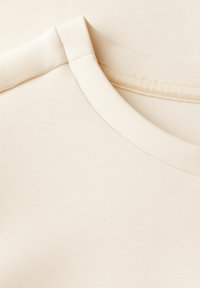 Beige Kurzarmhemd mit rundem Halsausschnitt, aus weichem, glattem Stoff gefertigt. Verfügt über eine dezente gerippte Textur und saubere Nähdetails.
