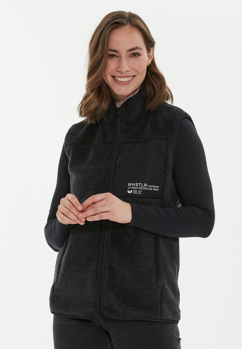 Mustavilla fleece-liivillä, jossa on korkea kaulus, etuvetoketju ja brändäys rinnassa. Pehmeä rakenne ja hihaton malli.