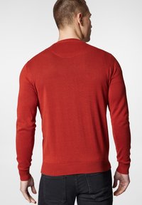 Czerwony sweter z dzianiny z długimi rękawami, ściągaczami przy mankietach i u dołu. Gładka faktura i okrągły dekolt. Widok z tyłu, ukazujący dopasowany krój.