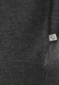 Dunkelgrauer gestrickter Stoff mit einem kleinen weißen Etikett, auf der rechten Seite mit einem runden Logo.