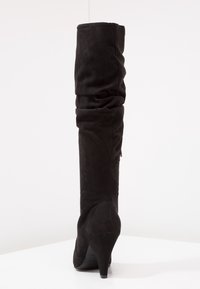 Botas negras de ante sobre la rodilla con un diseño holgado, punta afilada y tacón refinado. Textura suave con un detalle mínimo.