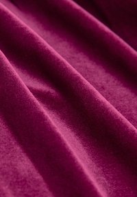 Tessut din catifea magenta profund, cu o textură moale, prezentând ondulații ușoare și strălucire, subliniind culoarea sa bogată și apariția netedă.